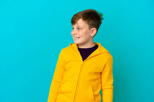 Little Redhead Boy Isolated Blue Background Looking Side Smiling — Stock Photo, Image