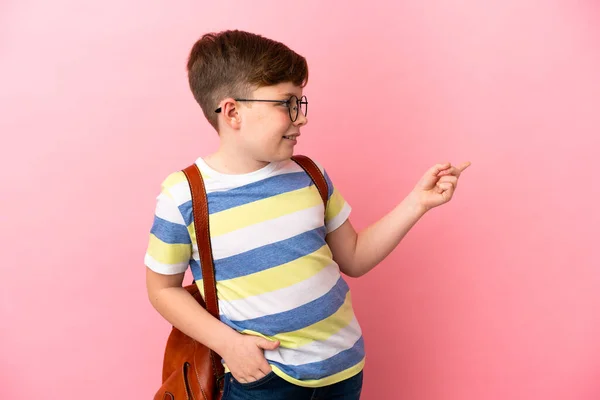红头发的白人小男孩被粉色背景隔离 手指指向侧面 展示了一种产品 — 图库照片
