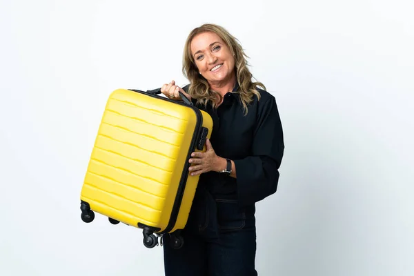 Middle aged blonde woman over isolated white background in vacation with travel suitcase