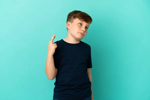 Μικρό Κοκκινομάλλικο Αγόρι Απομονωμένο Μπλε Φόντο Δάχτυλα Σταυρωμένα Και Ευχόμενος — Φωτογραφία Αρχείου