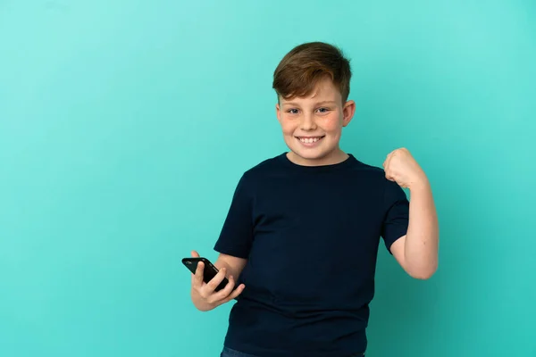 Petit Rouquin Isolé Sur Fond Bleu Avec Téléphone Position Victoire — Photo