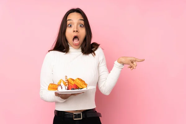 Young Brunette Woman Holding Waffles Isolated Pink Background Surprised Pointing — Stock Photo, Image