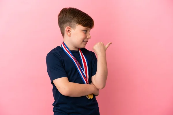 Little Redhead Boy Medals Isolated Pink Background Pointing Side Present — Stock Photo, Image