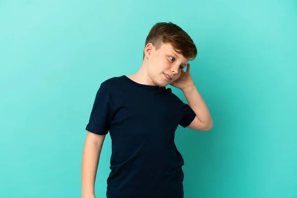 Ένα Μικρό Κοκκινομάλλικο Αγόρι Απομονωμένο Μπλε Φόντο Ακούγοντας Κάτι Βάζοντας — Φωτογραφία Αρχείου