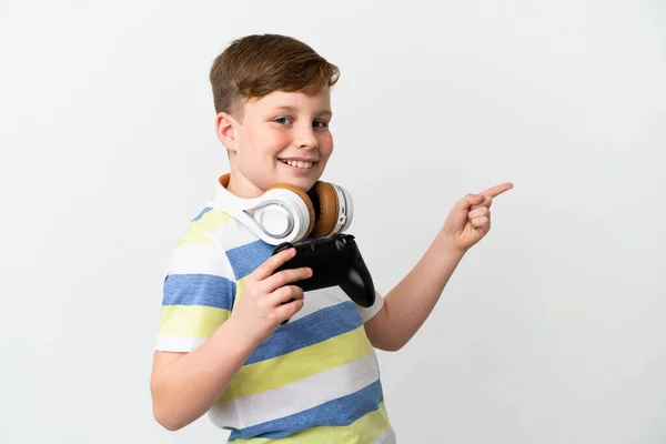 一个红头发的小男孩拿着一个用白色背景隔开的游戏垫 手指指向旁边 并展示了一个产品 — 图库照片