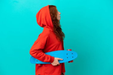 Genç kızıl saçlı kız mavi arka planda tek başına paten kayıyor.