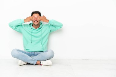 Caucasian handsome man sitting on the floor covering eyes by hands