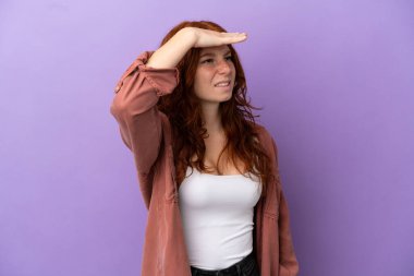 İzole edilmiş mor arka planda genç bir kızıl kız. Bir şeye bakmak için çok uzaklara bakıyor.