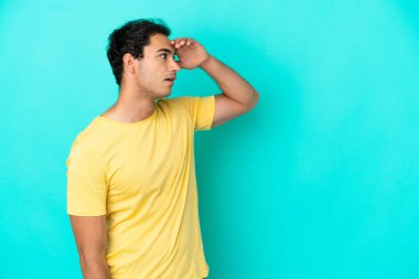 Kafkasyalı yakışıklı bir adam mavi arka planda, sürpriz bir ifadeyle yan yana bakarken.