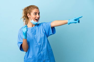 İzole edilmiş mavi arka planda aletleri tutan genç bir dişçi var.