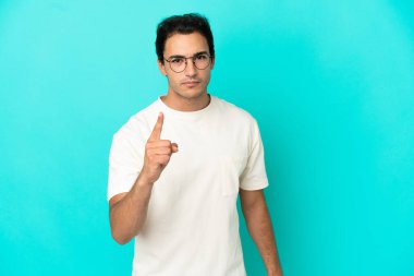 Kafkasyalı yakışıklı adam mavi arka planda hayal kırıklığına uğramış ve ön tarafı işaret ediyor.