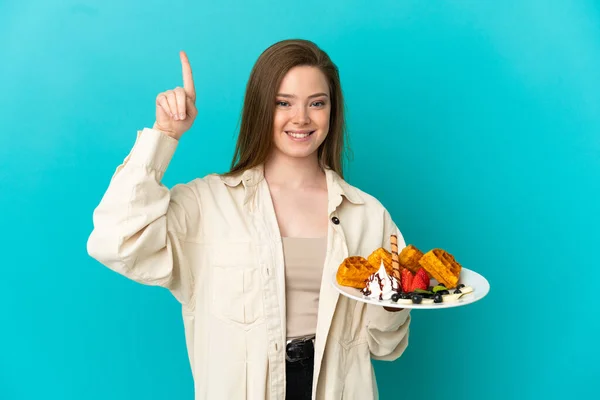 Adolescente Menina Segurando Waffles Sobre Isolado Fundo Azul Apontando Para — Fotografia de Stock