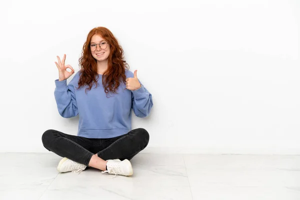 Teenager Zrzka Dívka Sedí Podlaze Izolované Bílém Pozadí Ukazující Znamení — Stock fotografie