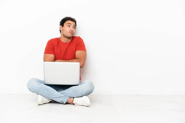 Caucasian Handsome Man Laptop Sitting Floor Making Doubts Gesture While — Fotografia de Stock