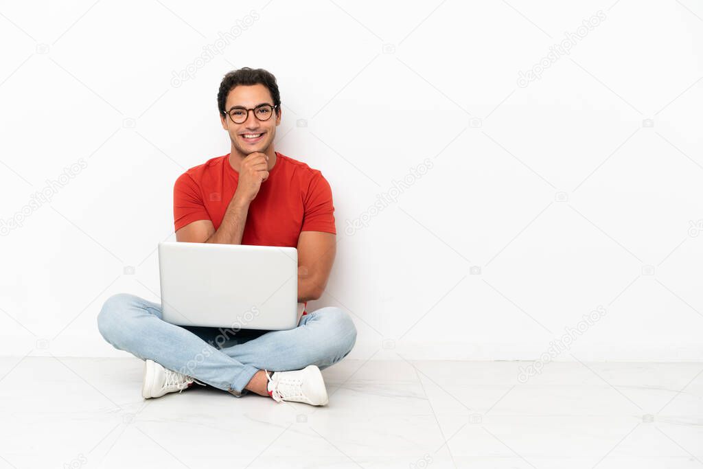 Caucasian handsome man with a laptop sitting on the floor with glasses and smiling