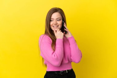 İzole edilmiş sarı arka plan üzerinde cep telefonu kullanan genç kız yana bakıyor ve gülümsüyor.