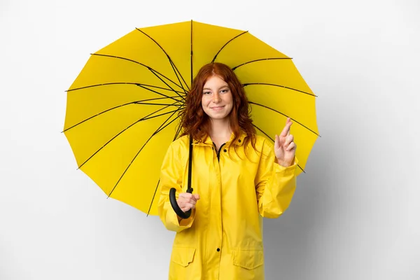 ティーンRedhead女の子雨防止コートと傘隔離上のホワイトバックグランドとともに指交差と願いますザベスト — ストック写真