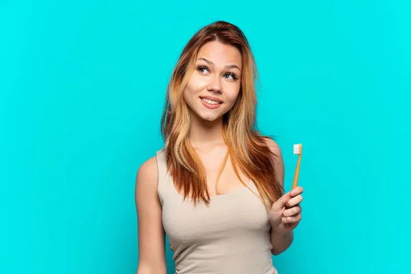 Adolescente Chica Cepillarse Los Dientes Sobre Aislado Fondo Azul Pensando —  Fotos de Stock