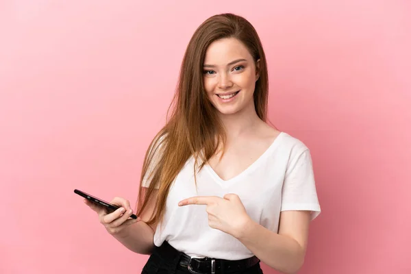Ragazza Adolescente Sfondo Rosa Isolato Utilizzando Telefono Cellulare Indicandolo — Foto Stock