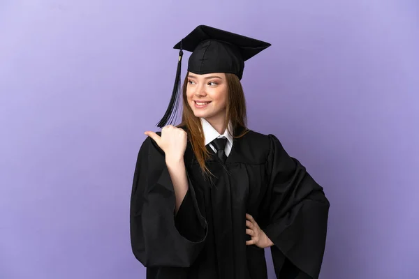 Young university graduate over isolated purple background pointing to the side to present a product