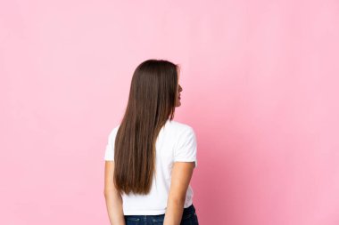 Genç Uruguaylı kadın pembe arka planda izole edilmiş ve arkasına bakıyor.