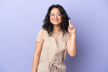 Restoran Asyalı garson mor arka planda izole edilmiş ve en iyinin işareti olarak parmağını kaldırıyor.