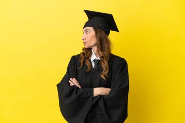 Orta yaşlı üniversite mezunu. Sarı arka planda izole edilmiş. Kolları bağlı ve mutlu.