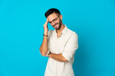 Kafkasyalı genç adam mavi arka planda izole edilmiş, baş ağrısı var.