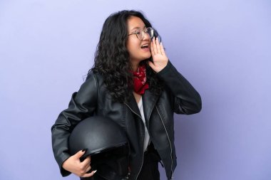 Motosiklet kasklı genç Asyalı kadın mor arka planda izole edilmiş ağzı sonuna kadar açık bağırıyor.