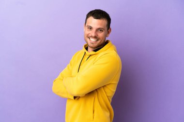 İzole edilmiş mor arka planı olan Brezilyalı bir adam kollarını kavuşturup ileriye bakıyor.