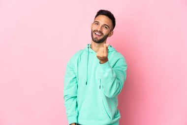 Pembe arka planda izole genç beyaz adam para hareketi yapıyor.