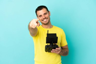 Brezilyalı bir adam uzaktan kumandayla izole edilmiş mavi arkaplanı kontrol ediyor mutlu bir ifadeyle ön tarafı işaret ediyor