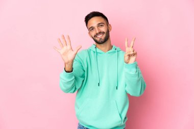 Pembe arka planda izole edilmiş genç beyaz adam yediyi parmaklarıyla sayıyor.