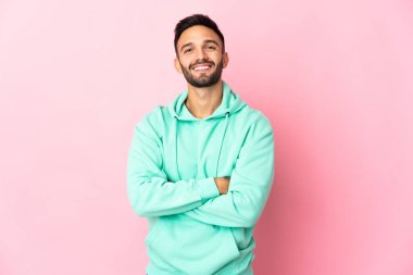 Pembe arka planda izole edilmiş genç beyaz adam kollarını ön cephede çapraz tutuyor.