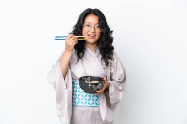 Beyaz arka planda izole edilmiş kimono giyen genç Asyalı kadın elinde çubuklu erişte kasesi tutuyor.