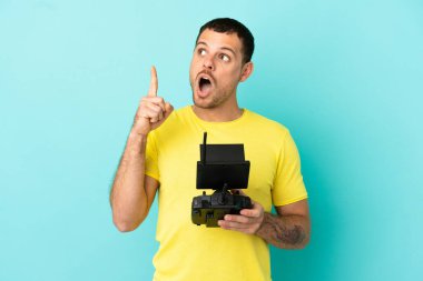 Brezilyalı bir adam uzaktan kumandayla izole edilmiş mavi arkaplanı kontrol ediyor.