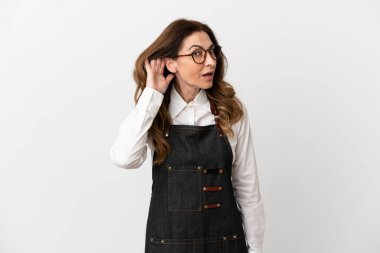 Restorandaki orta yaşlı garson kadın beyaz arka planda izole edilmiş bir şekilde elini kulağına koyarak bir şeyler dinliyor.