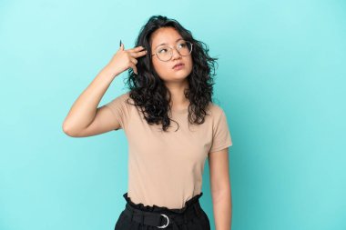 Asyalı genç bir kadın mavi arka planda izole edilmiş ve intihar jesti yapmada sorun yaşıyor.