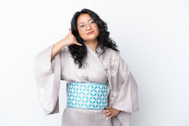 Kimono giyen genç Asyalı kadın beyaz arka planda izole edilmiş bir şekilde telefon jesti yapıyor. Bana geri dönüş işareti ver.