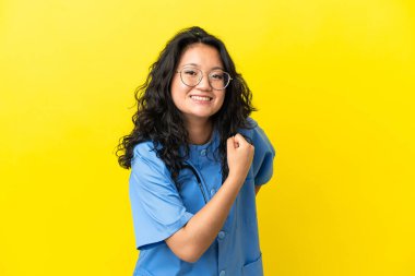 Genç cerrah Asyalı kadın sarı arka planda izole edilmiş zaferi kutluyor.