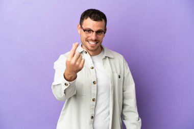 İzole edilmiş mor arka planı olan Brezilyalı adam para hareketi yapıyor.