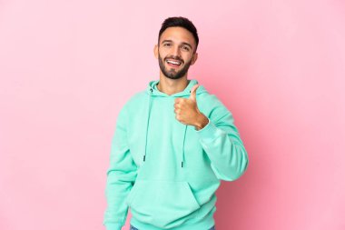 Pembe arka planda izole edilmiş genç beyaz bir adam baş parmak hareketi yapıyor.