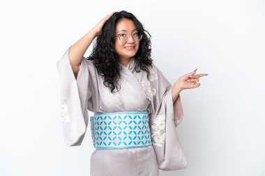 Kimono giyen genç Asyalı kadın beyaz arka planda izole edilmiş, şaşırmış ve parmağını yana doğru uzatmış.