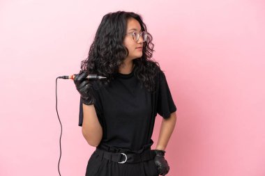 Dövme sanatçısı Asyalı kadın pembe arka planda izole edilmiş, yan tarafa bakıyor.