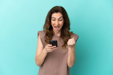 Mavi arka planda izole edilmiş orta yaşlı beyaz kadın şaşırdı ve bir mesaj gönderiyor.