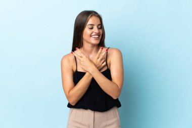 Mavi arka planda izole edilmiş genç Uruguaylı kadın gülümsüyor ve zafer işareti gösteriyor.