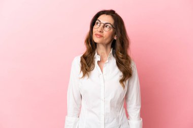 Orta yaşlı beyaz kadın pembe arka planda izole edilmiş bir şekilde yukarı bakarken bir fikir düşünüyor.