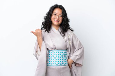 Kimono giyen genç Asyalı kadın beyaz arka plana izole edilmiş bir ürün sunmak için yan tarafı işaret ediyor.