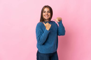 Pembe arka planda izole edilmiş genç Uruguaylı kadın bir ürünü sunmak için kenarı işaret ediyor.