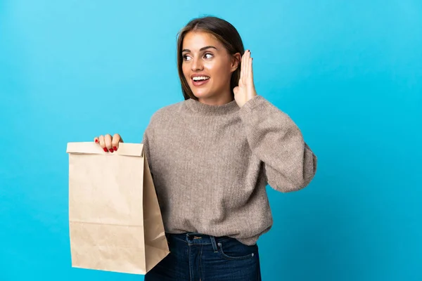 女人拿着一包蓝色背景的外卖食品 用手捂住耳朵听着什么 — 图库照片